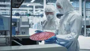 Two scientists in sterile suits inspecting a silicon wafer removed from a soldering jet printer in a semiconductor production facility.