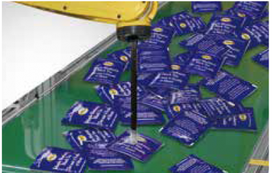 blue teabags on a green conveyor are picked by a yellow and black robot arm 