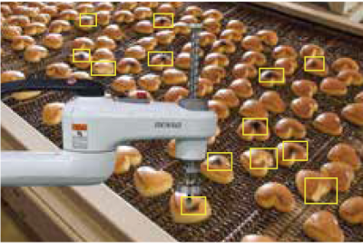 lots of heart-shaped baked items on a conveyor are picked by a robot arm