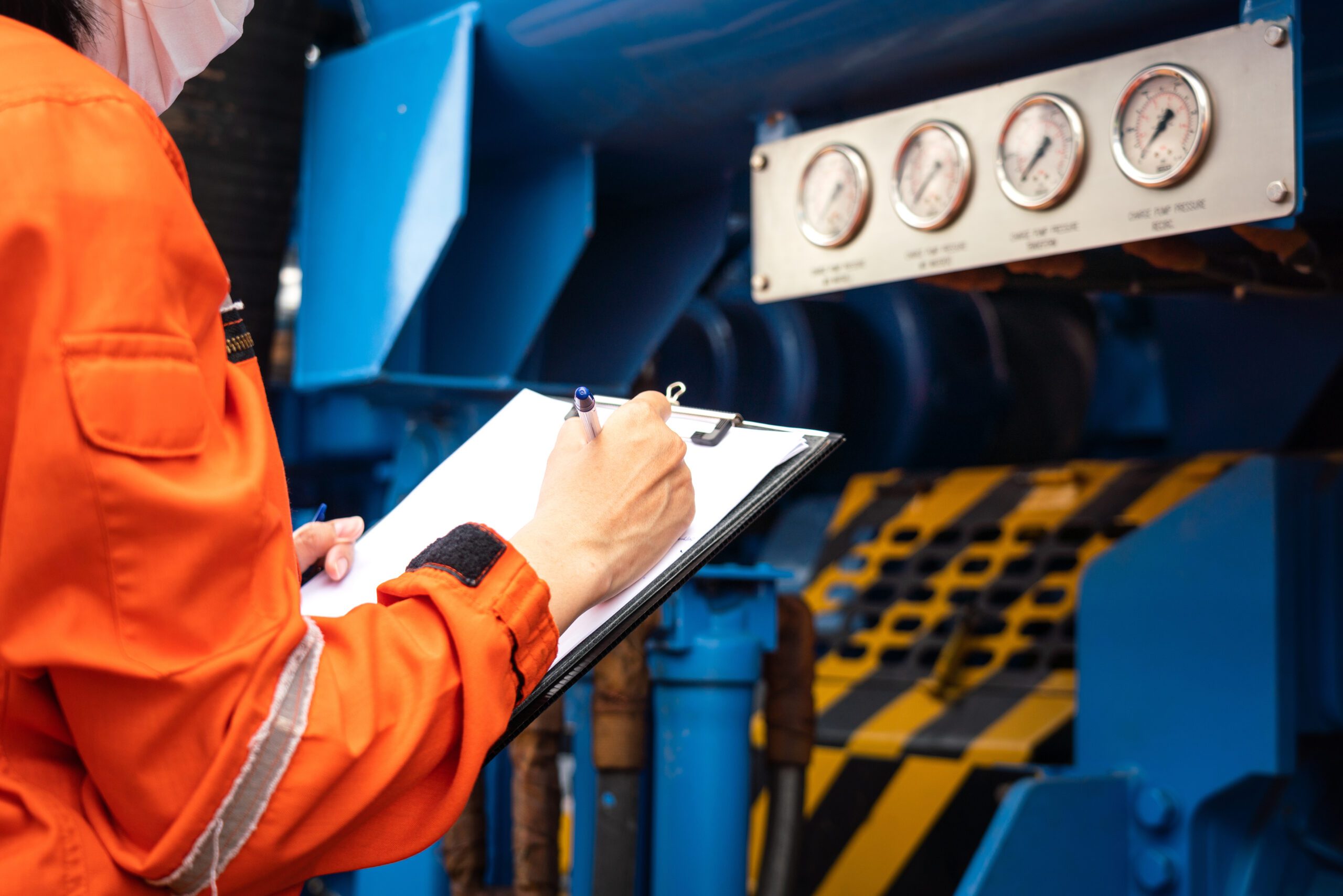 An engineer is recording pressure level of the pumping unit's gauge at refinery processing plant. Industrial working action scene photo, selective focus.