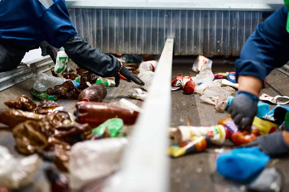 Worker sorts trash on conveyor belt at waste management recycling plant