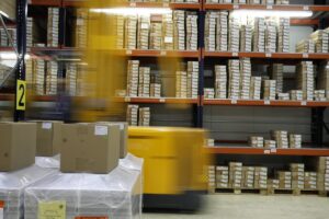 a forklift truck drives past stacked shelves insides a warehouse