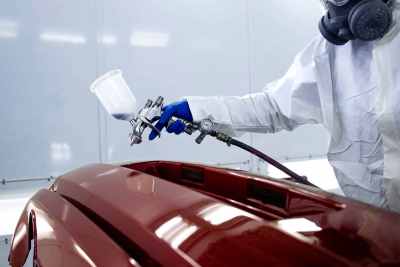 Automotive factory worker spray painting car body panel red