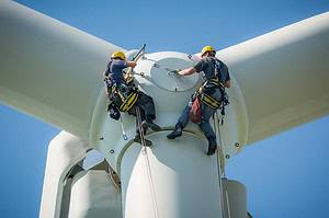 Inspection engineers preparing to rappel down a rotor blade of a wind turbine in a wind farm on a clear day with blue sky