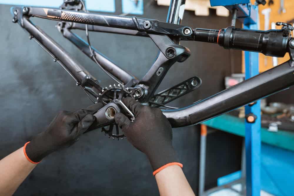 Bicycle frame production a mechanic's hand wearing gloves installing the right crank arm on the bottom bracket with a workshop background