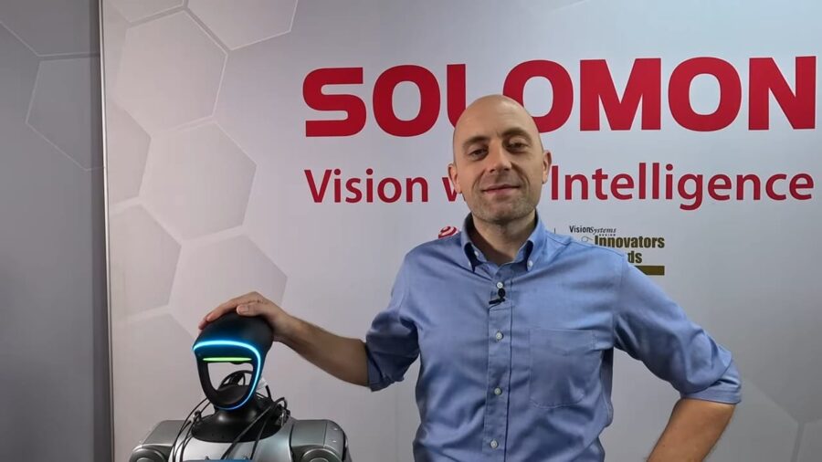 YouTube video thumbnail of Kyle from Solomon Technology standing next to the Solomon humanoid robot. Kyle is wearing a blue shirt, and the robot is silver.