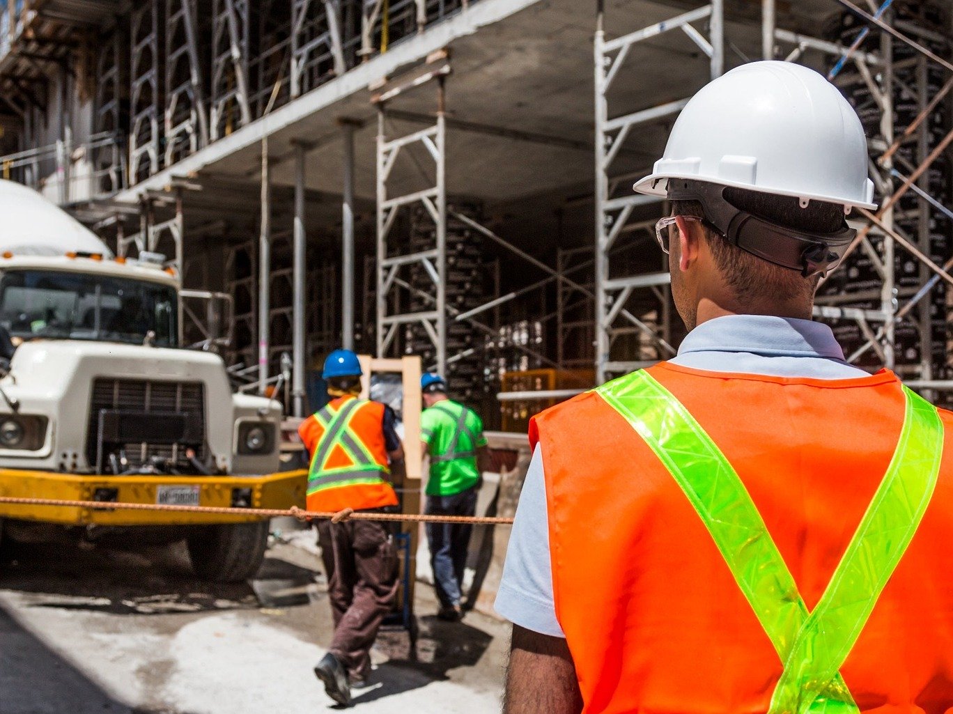 three construction workers wearing hi vis jackets at a construction site in front of a cement truck