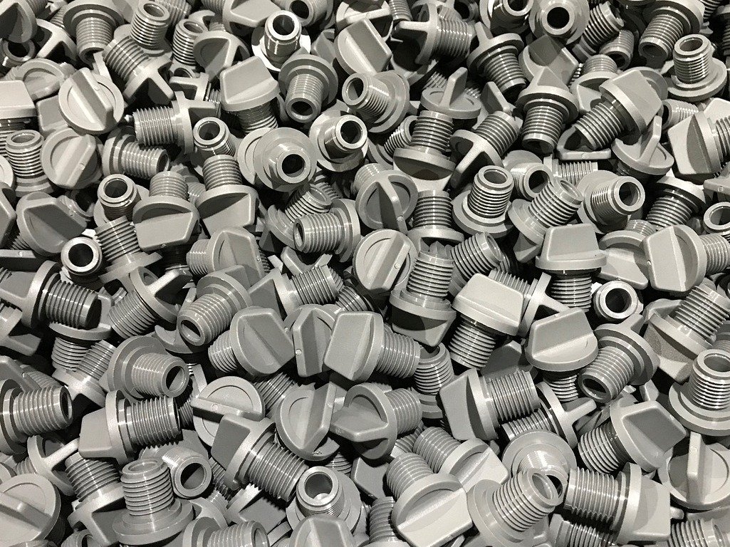Close-up of a dense pile of injection-molded, gray threaded plastic components, demonstrating the use of AI vision for quality inspection and defect detection in the petrochemicals, plastics, and rubber industry.
