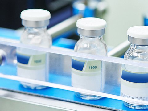 Small glass medical vials containing a liquid moving along a sterile, blue and white conveyor belt, representing the use of AI vision for inspection, labeling verification, and fill-level checks in the pharmaceuticals and medical industry.
