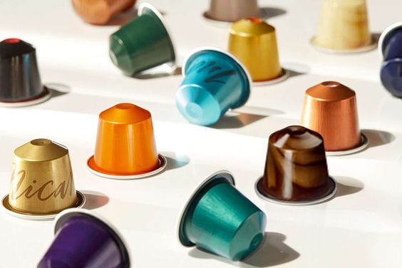 Coffee capsules in different colors and orientations illustrate the reflective aluminum surfaces and visual variations involved in automated coffee capsule inspection.