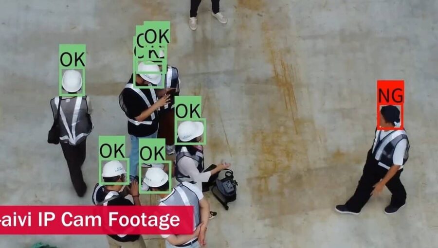An overhead view of construction workers wearing safety vests and hard hats, with an AI safety inspection system detecting PPE compliance. Green bounding boxes with "OK" labels indicate compliant workers, while a red box with an "NG" label highlights a worker without a hard hat.
