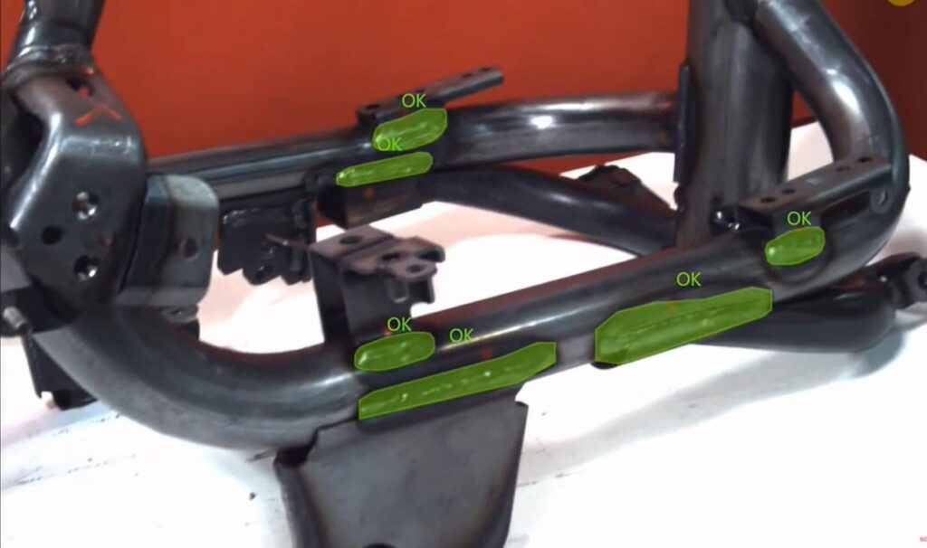 Welding Defect Inspection using META-aivi AR + AI An industrial metal frame assembly undergoing welding inspection. The AR interface overlays green segmentation masks and "OK" labels onto verified weld joints, demonstrating how AI-powered defect detection supports human-AI collaboration and improves inspection accuracy in smart manufacturing.