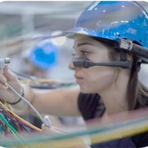 female worker wearing blue hardhat inspects electrical wiring using RealWear AR glasses