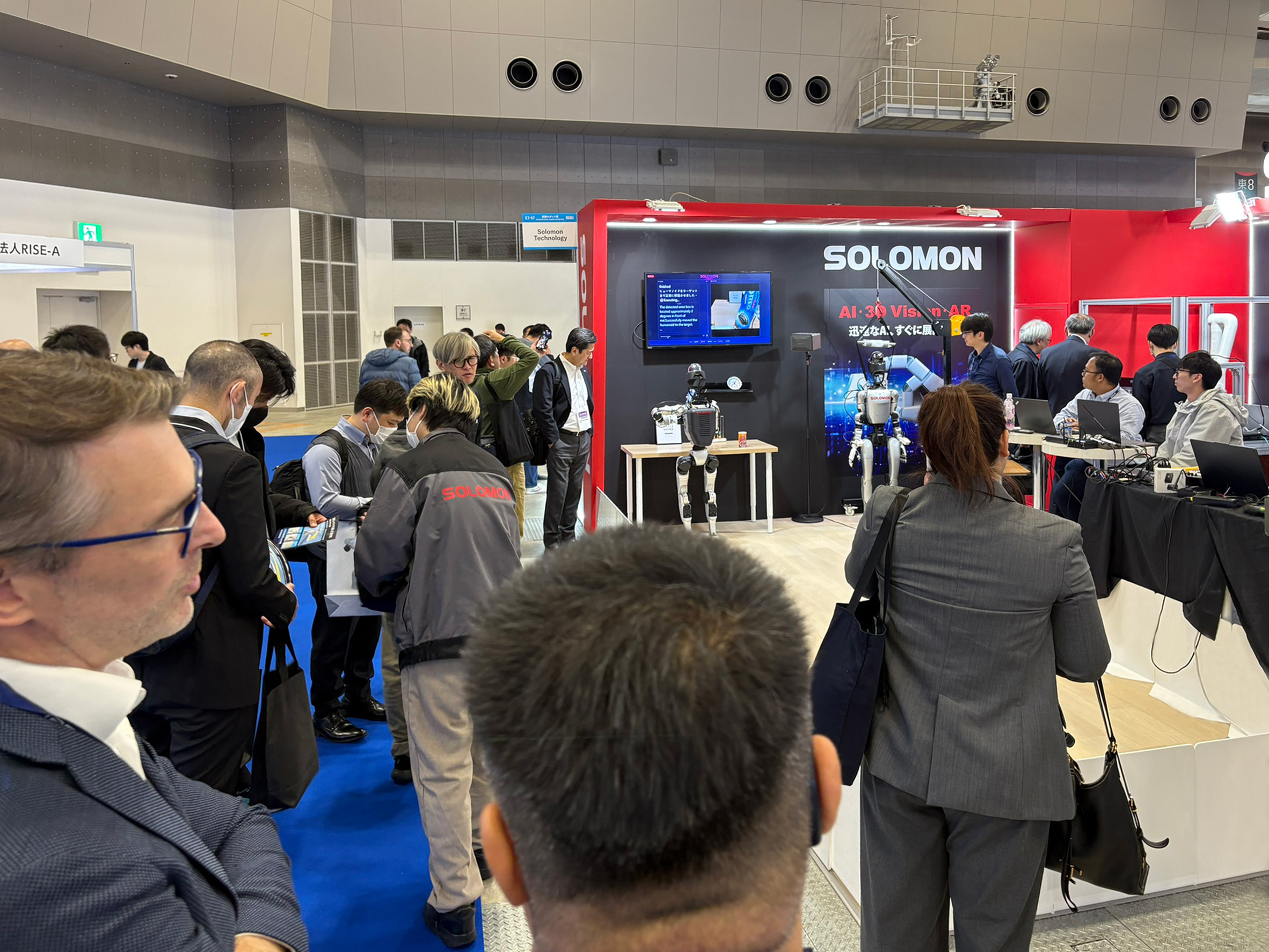 Solomon AI Humanoid Robot Demo at iREX 2025 Industry attendees gathering at the Solomon booth at iREX 2025 to view the latest humanoid robot and AI vision technologies. The booth features live demonstrations of physical AI agents performing real tasks.