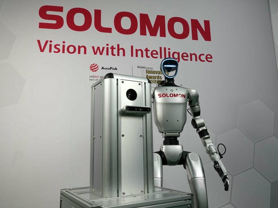 News Solomon humanoid robot with AI vision and an AMR in front of the Solomon logo and slogan in a warehouse.