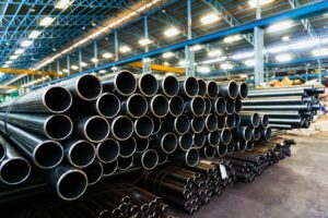 A large, complex stack of black steel pipes and metal tubing in a manufacturing warehouse, representing the inventory management challenge solved by AR + AI.