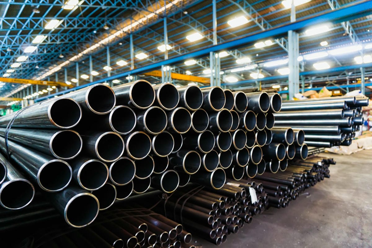 A large, complex stack of black steel pipes and metal tubing in a manufacturing warehouse, representing the inventory management challenge solved by AR + AI.